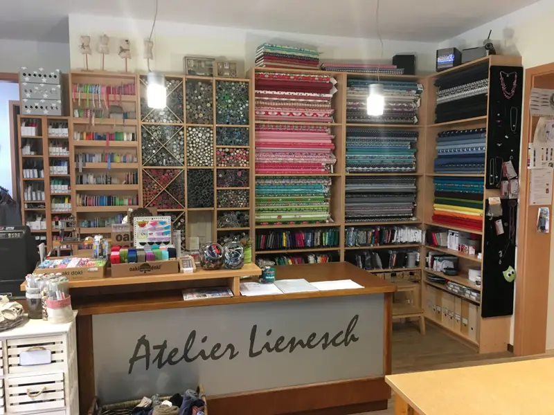 Ladentheke mit dem Schriftzug „Atelier Lienesch“ vor Stoff- und Kurzwarenregalen
