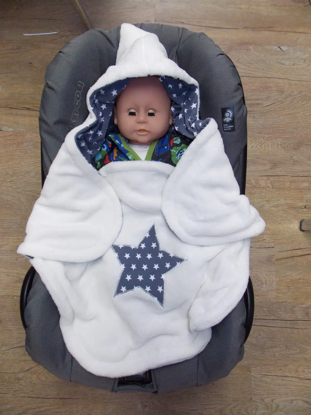 Weiße Babydecke mit Stern, um eine Puppe in der Babyschale gelegt
