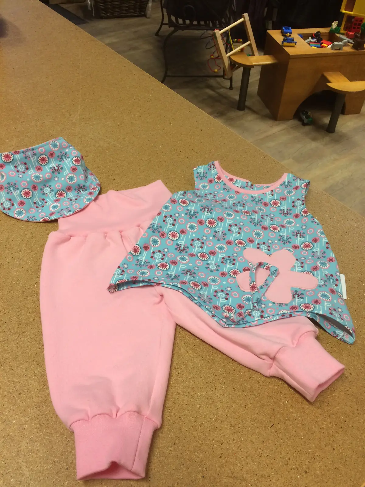 Rosa Kinderhose, gemustertes Oberteil und Mütze auf dem Tisch